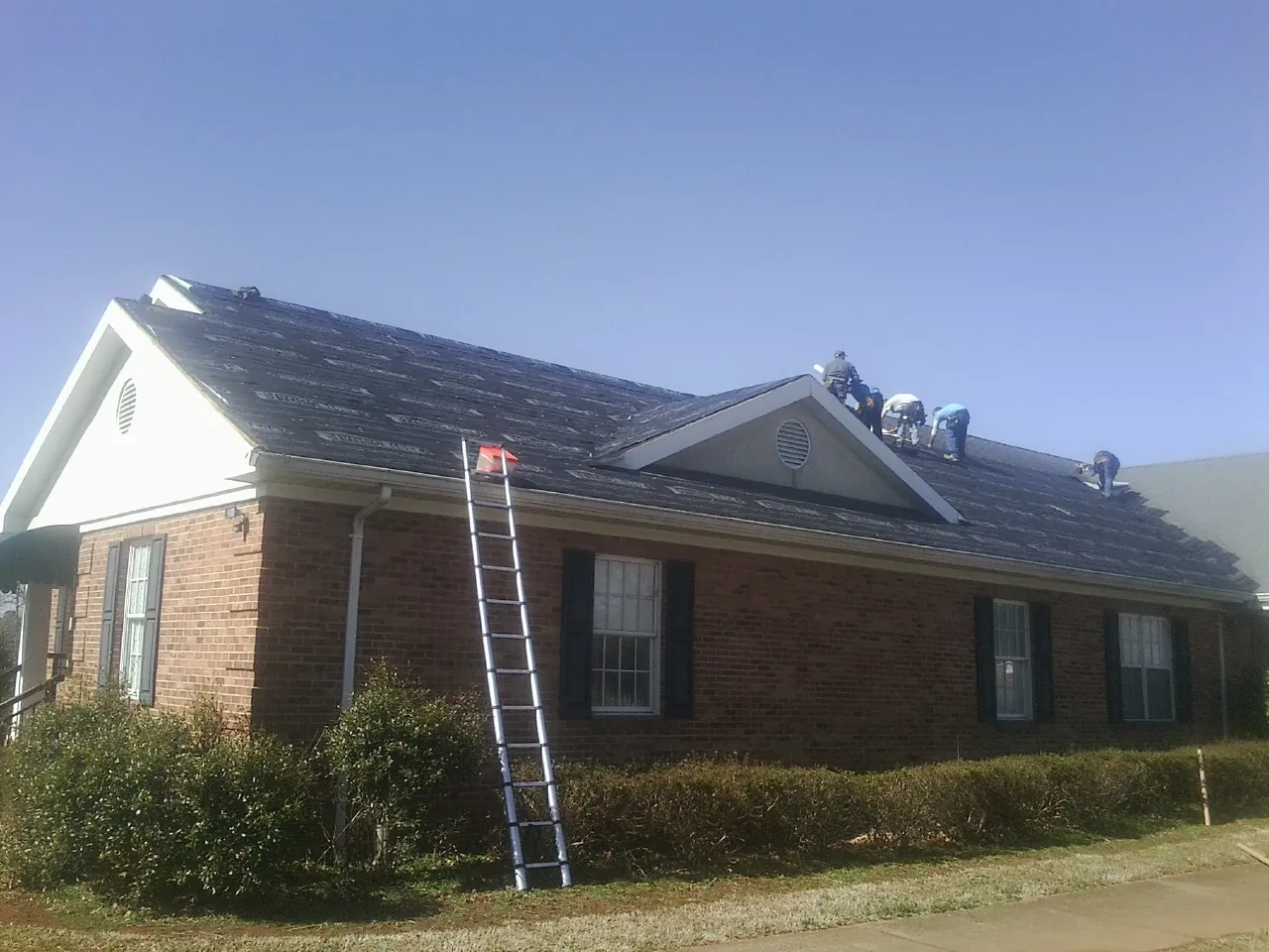 Crew tearing shingles off a brick ranch roof with a ladder set — Emergency Roof Repair work by our crew in La Jose