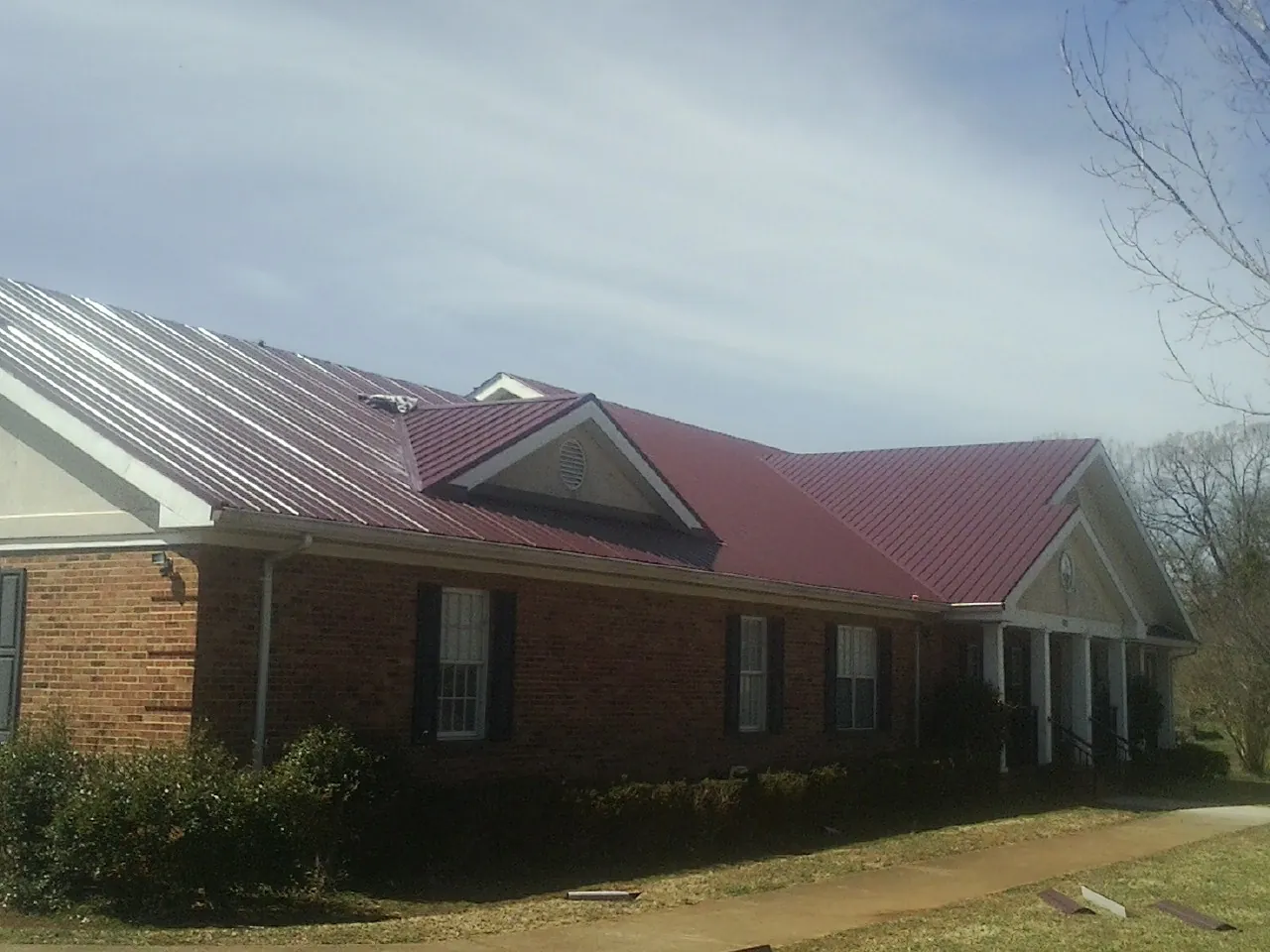 Red metal roof with gabled entries on a long brick building, from a Hail Damage Roof Repair job in La Jose
