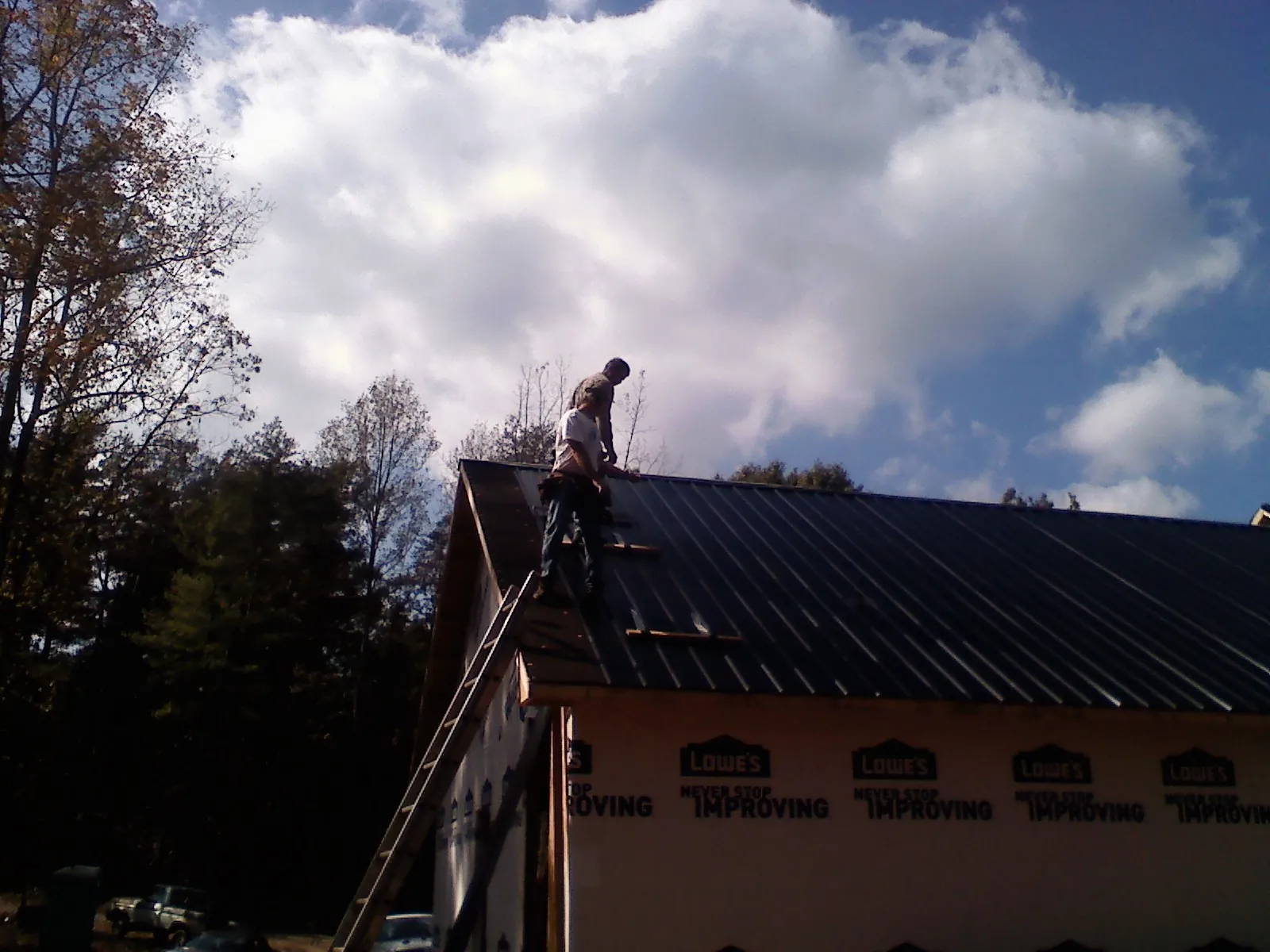 Roofer fastening dark metal panels high against a cloudy sky, from a Roof Inspection job in La Jose