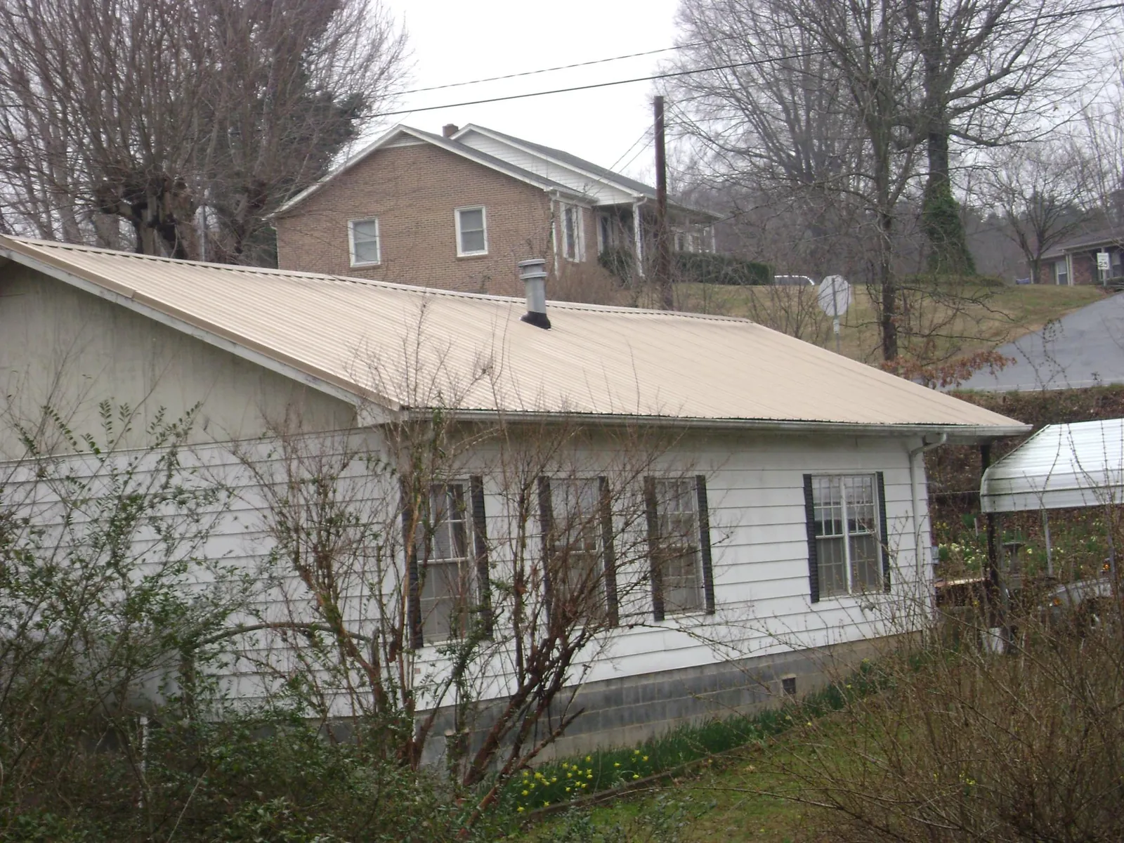 Tan metal roof on a white sided house set into a hillside — Commercial Roofing by Roofing Brothers in La Jose